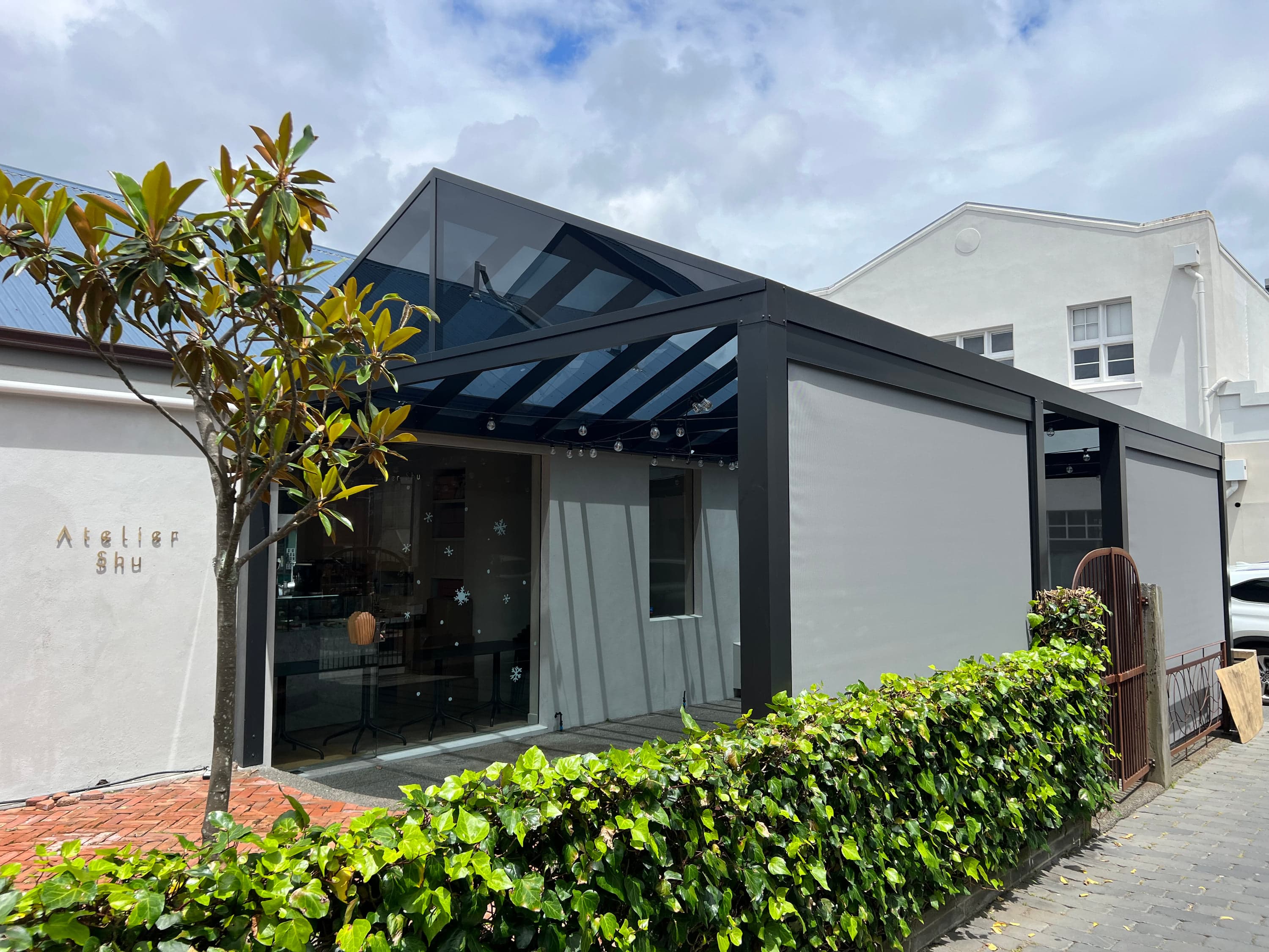 Dark-tint acrylic gable canopy across the Atelier Shu Cafe frontage in Newmarket
