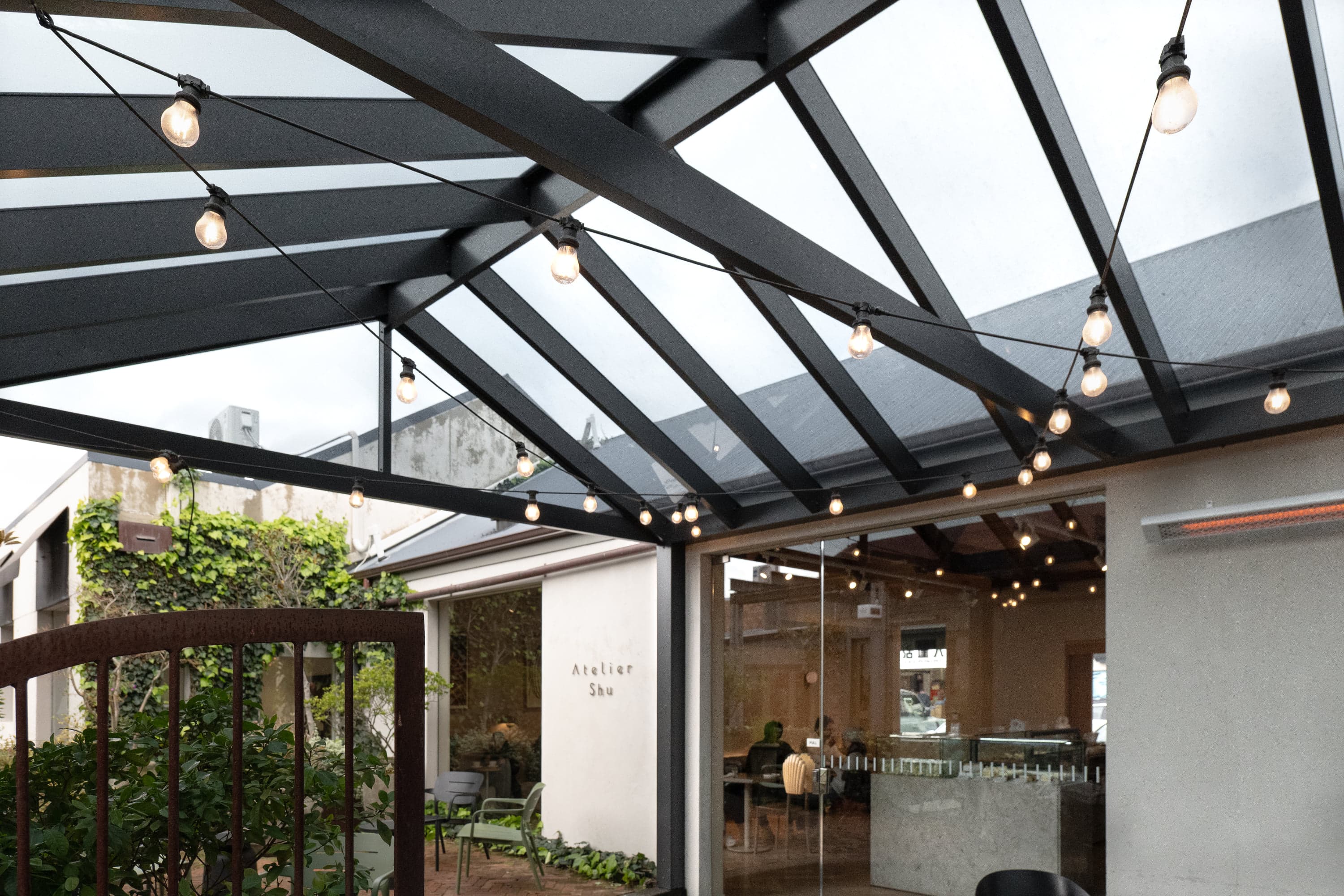 Dark-tint acrylic roofing and exposed gable frame above Atelier Shu Cafe seating