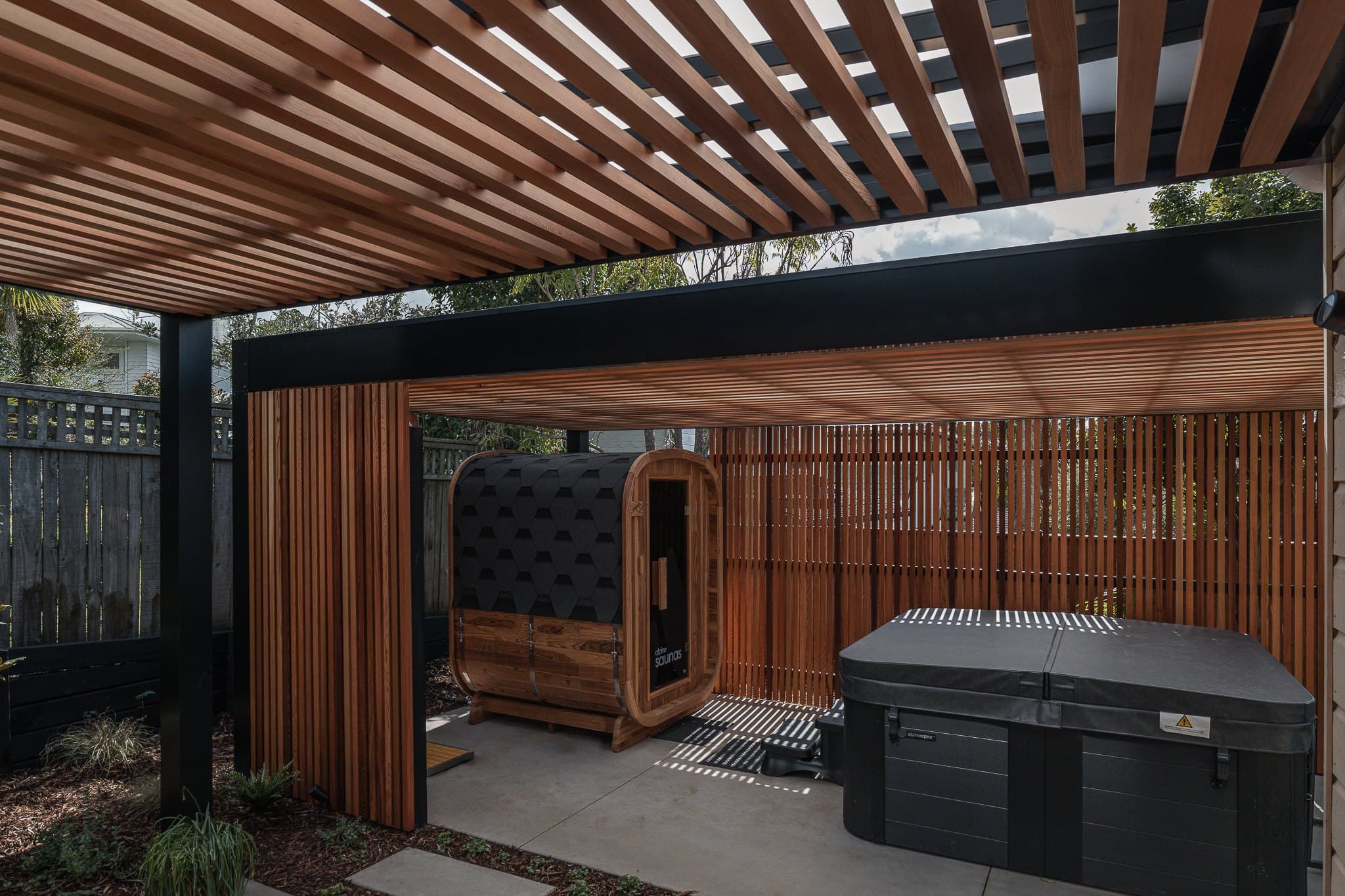 Satin-black pergola with cedar battens above a spa and sauna in a Milford garden