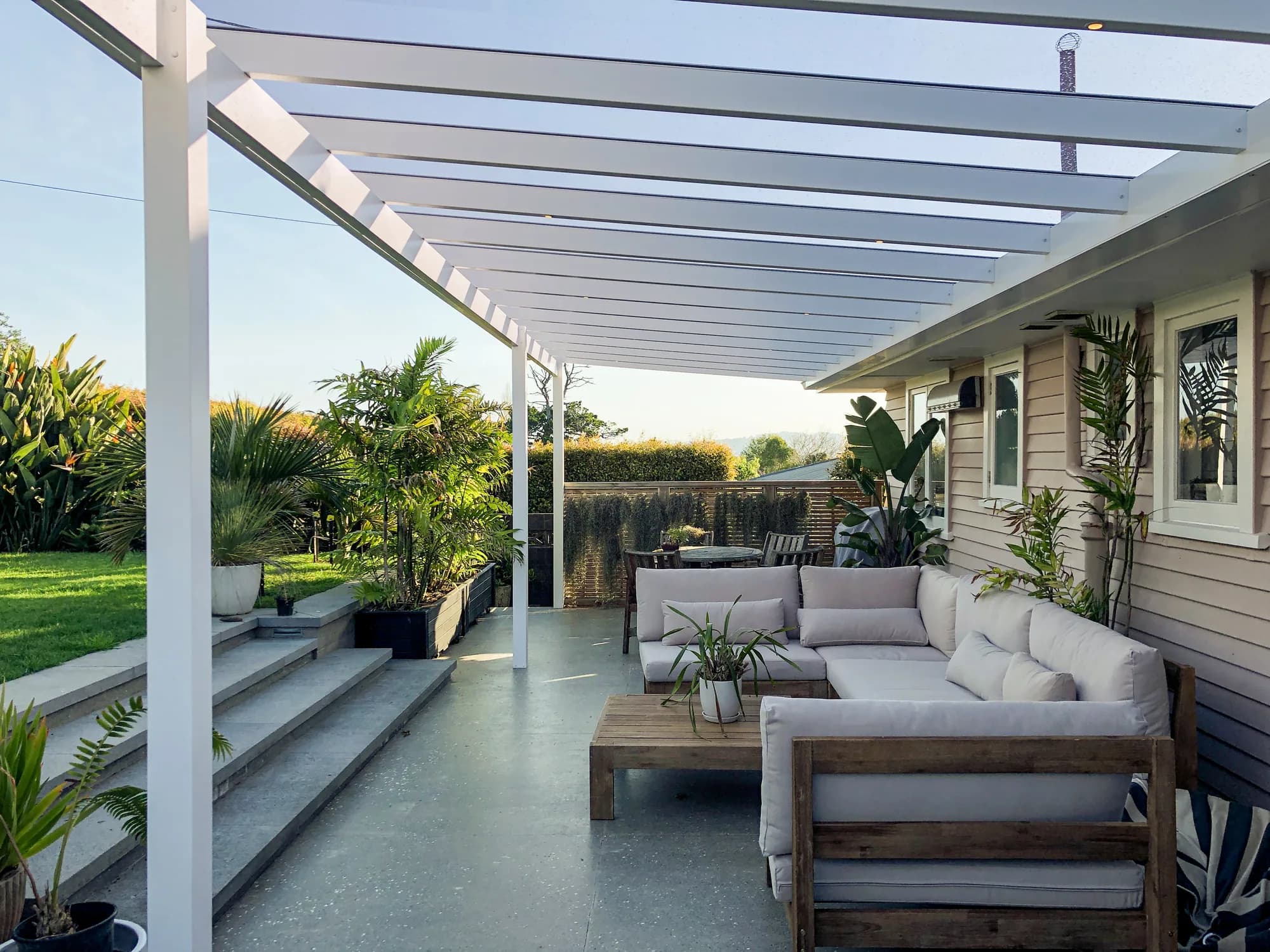 White pitched acrylic pergola covering a ground-level patio beside a weatherboard home